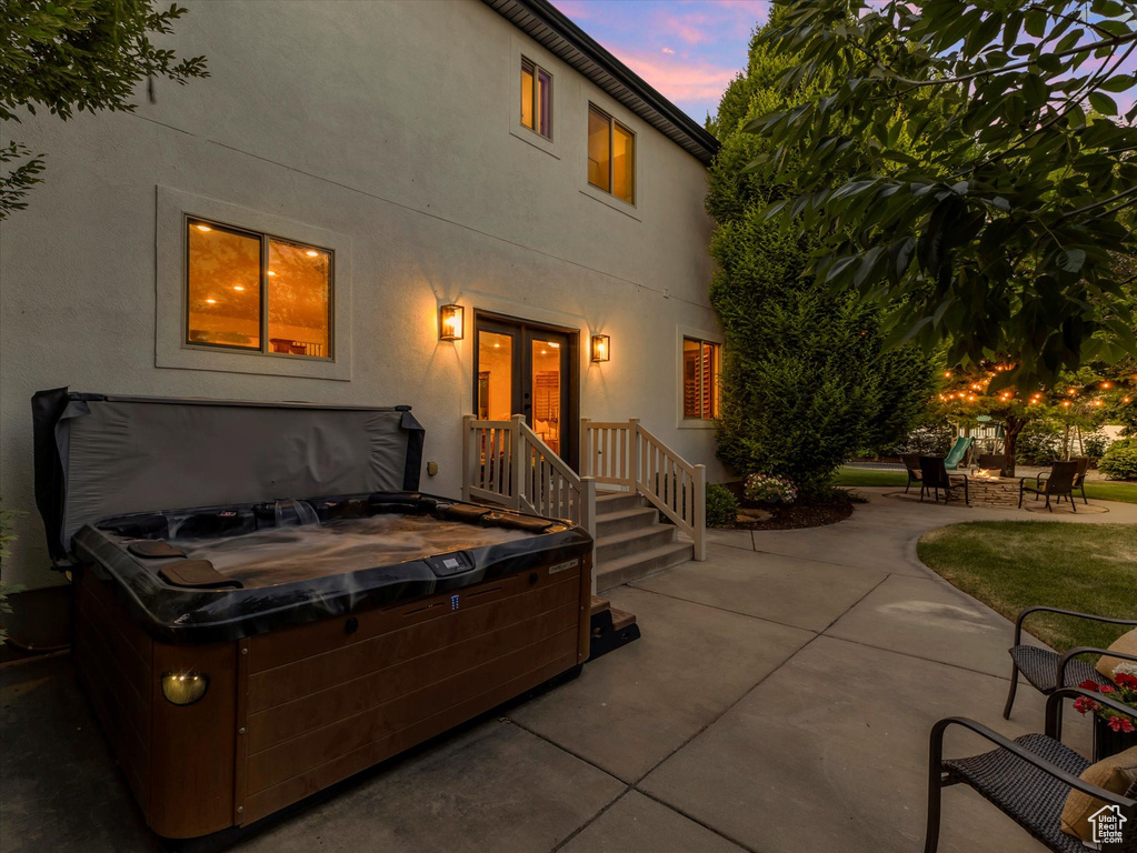 Back of property at dusk featuring a hot tub, a patio, stucco siding, and an outdoor fire pit