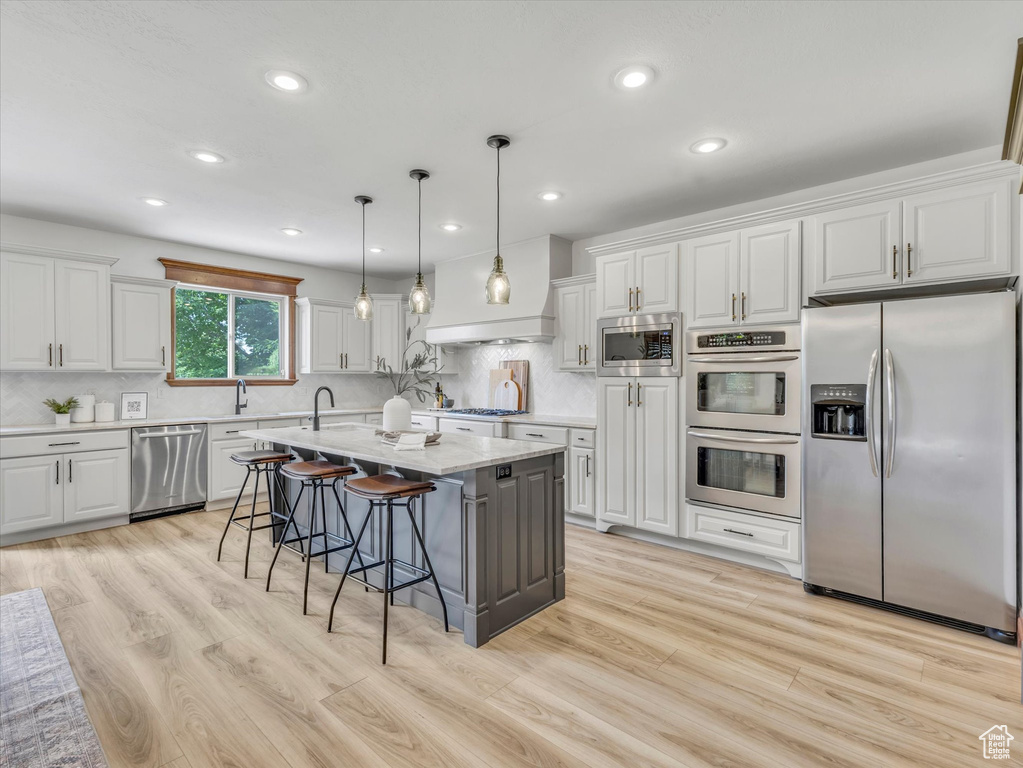 Kitchen featuring stainless steel appliances, a breakfast bar area, white cabinets, a kitchen island with sink, and backsplash