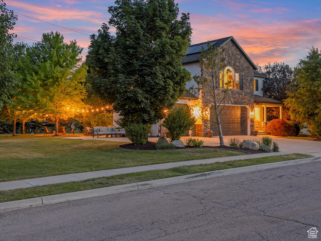 View of front of property with stone siding, an attached garage, roof mounted solar panels, concrete driveway, and an outdoor hangout area