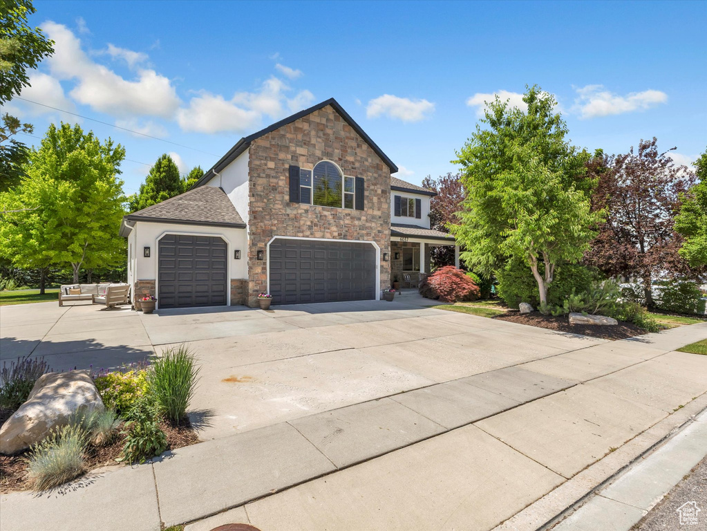 Traditional-style house with stone siding, concrete driveway, stucco siding, an attached garage, and a shingled roof