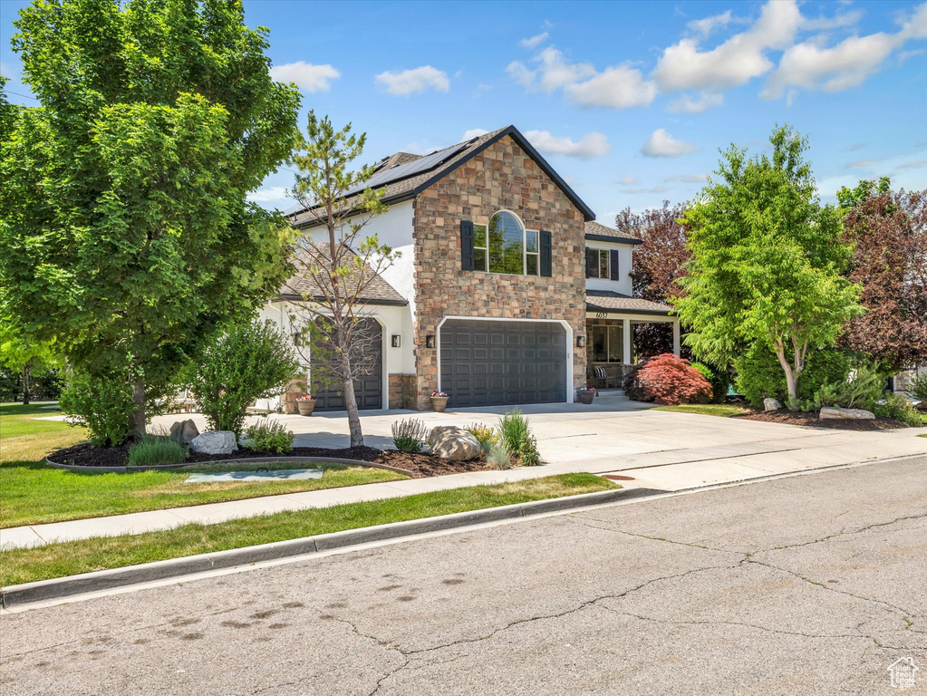 Traditional home with stone siding, an attached garage, concrete driveway, and roof mounted solar panels