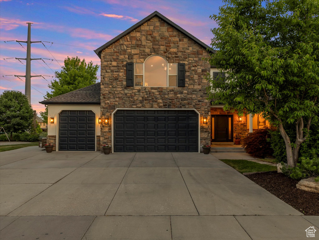 View of front of property with stone siding, driveway, an attached garage, and stucco siding