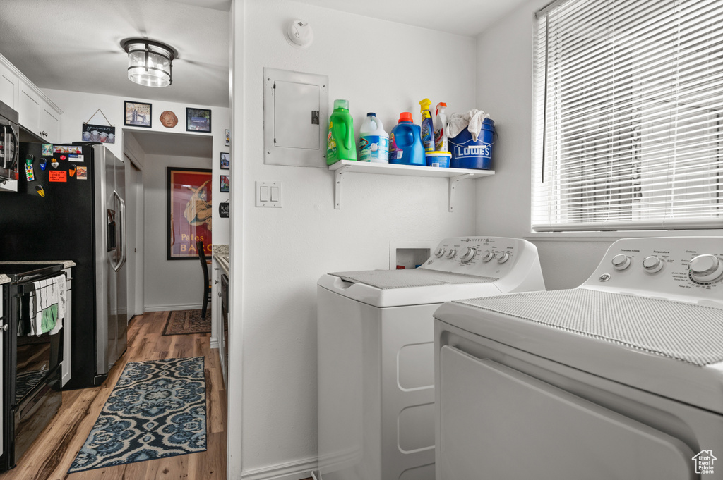 Laundry room with electric panel, independent washer and dryer, and light wood-style floors