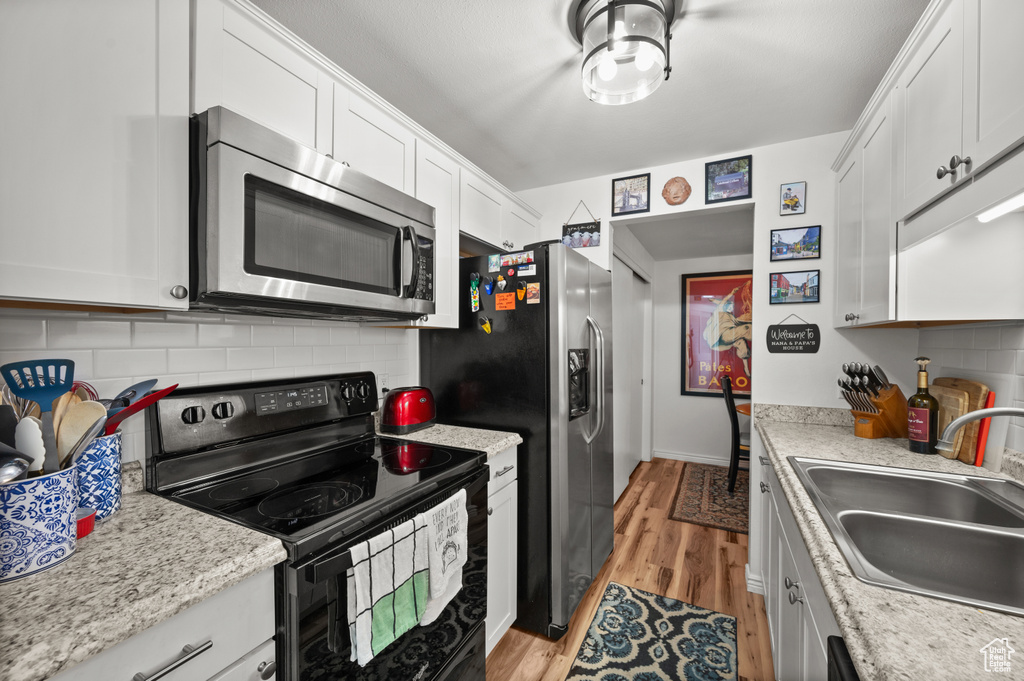 Kitchen featuring stainless steel appliances, decorative backsplash, light wood finished floors, and white cabinetry