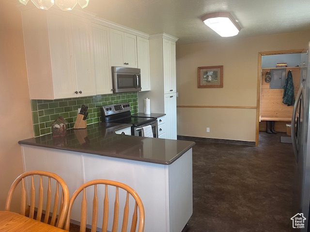 Kitchen featuring stainless steel appliances, dark countertops, backsplash, and white cabinetry