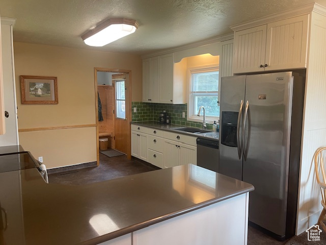 Kitchen with appliances with stainless steel finishes, backsplash, a textured ceiling, dark countertops, and white cabinetry