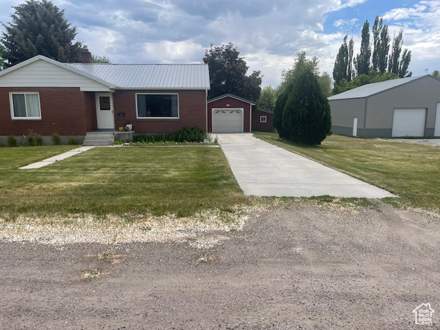 Single story home featuring an outbuilding, driveway, brick siding, a chimney, and a front yard