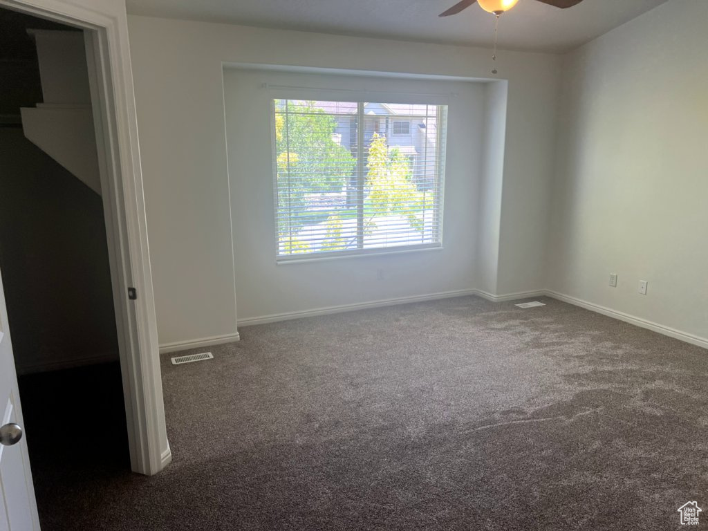 Unfurnished bedroom with dark carpet, multiple windows, and ceiling fan
