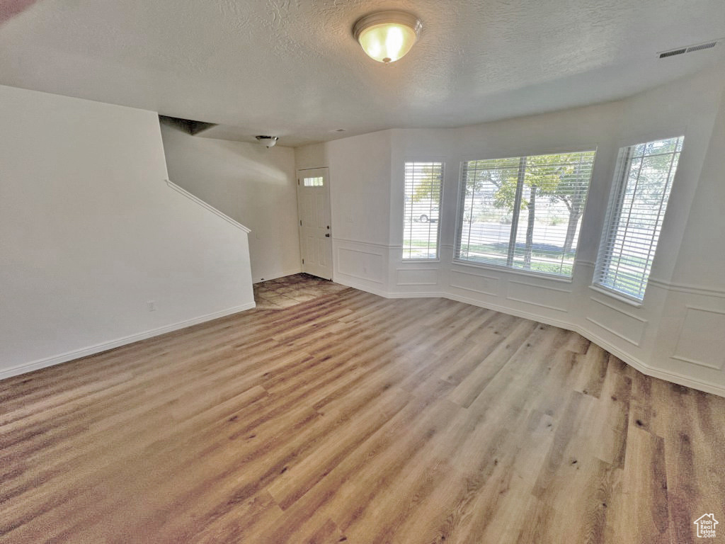 Unfurnished living room with a textured ceiling, light wood-style floors, wainscoting, and a decorative wall