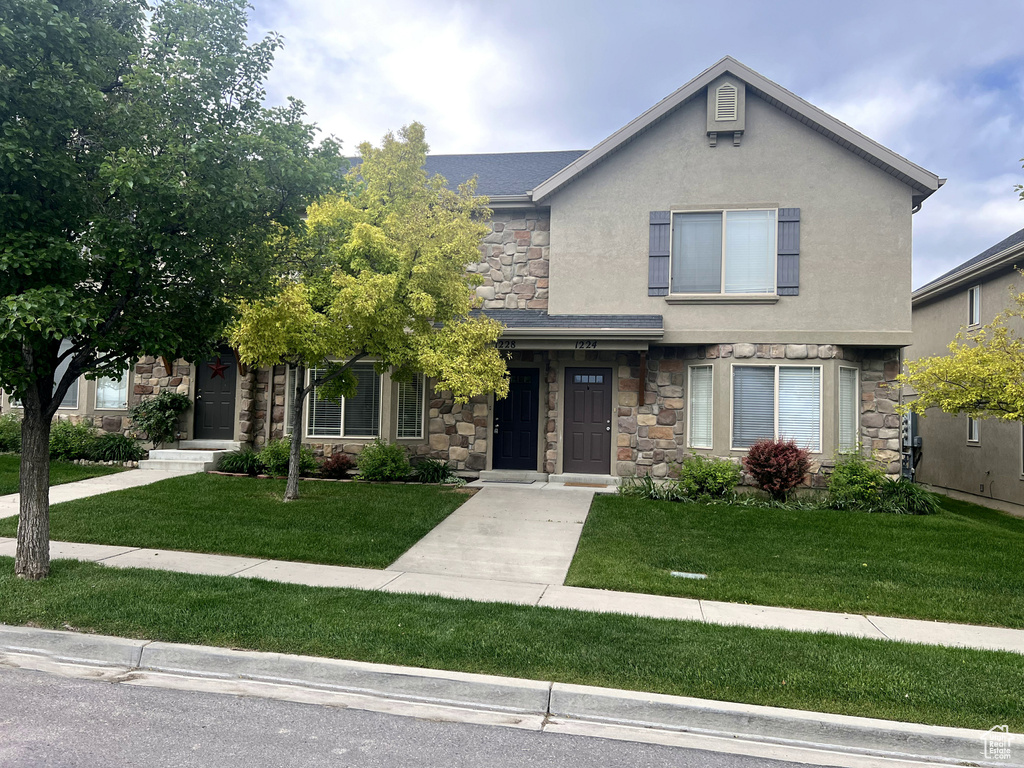 View of front facade featuring stone siding, stucco siding, and a front lawn