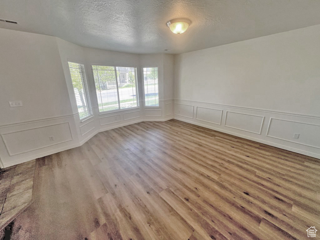 Empty room with a decorative wall, wood finished floors, a textured ceiling, and wainscoting