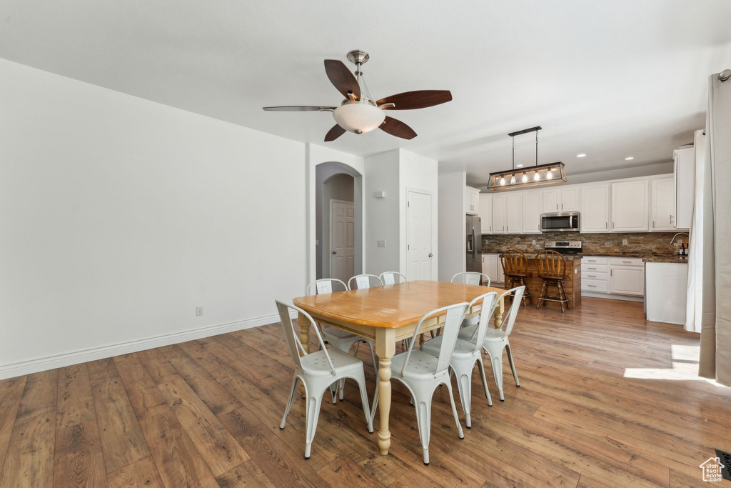 Dining room with arched walkways, ceiling fan, light wood-style floors, baseboards, and recessed lighting