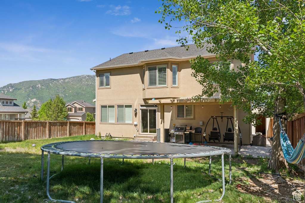 Back of house with a trampoline, stucco siding, a mountain view, and a pergola