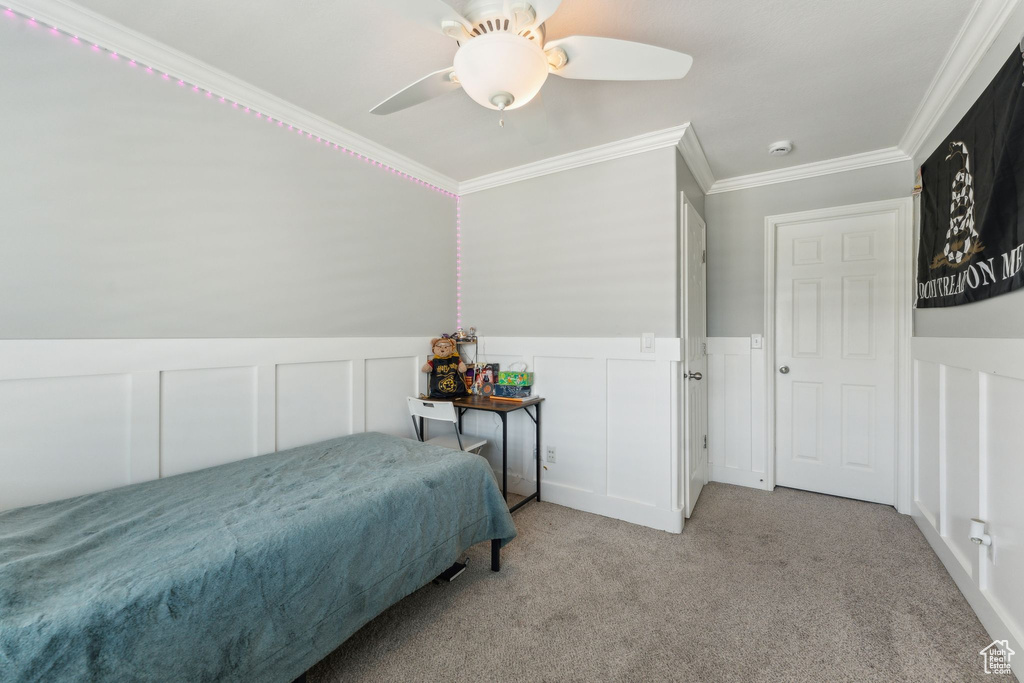 Bedroom with a decorative wall, carpet flooring, crown molding, a wainscoted wall, and a ceiling fan