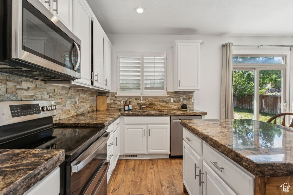 Kitchen with stainless steel appliances, a sink, backsplash, white cabinets, and light wood-type flooring