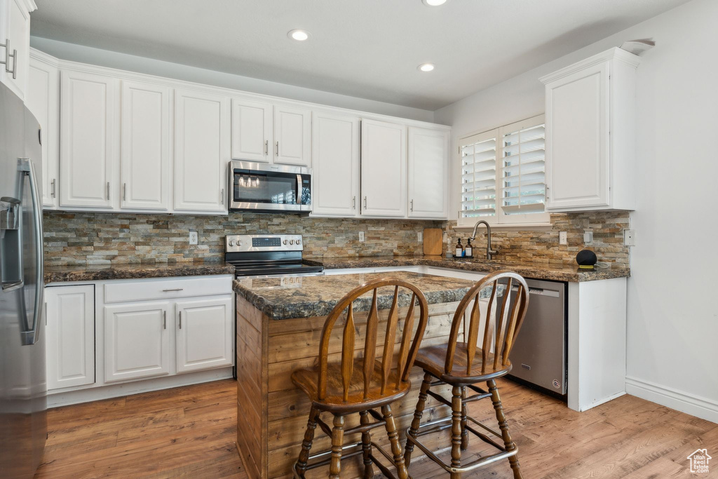 Kitchen with stainless steel appliances, recessed lighting, white cabinets, light wood-style floors, and backsplash