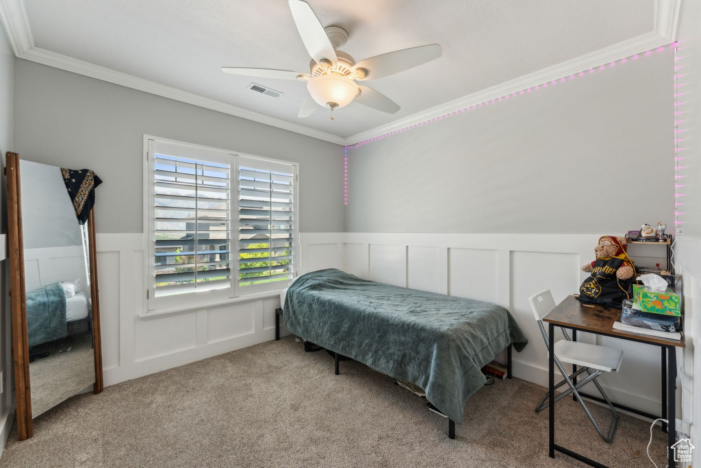 Carpeted bedroom with ornamental molding, a decorative wall, a wainscoted wall, and ceiling fan