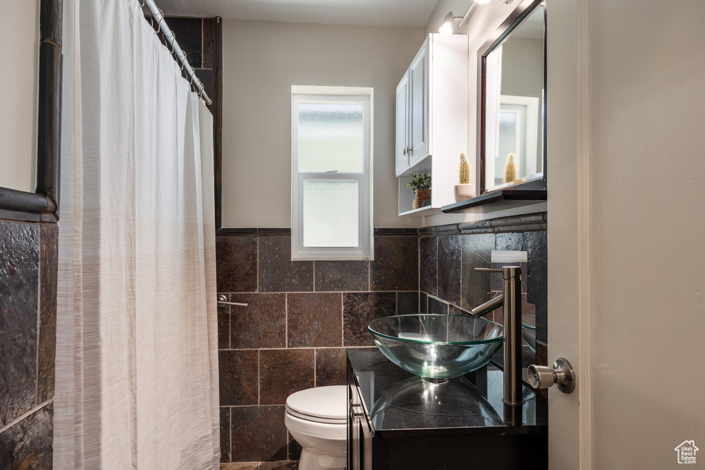Full bath featuring tile walls, vanity, a shower with shower curtain, and a wainscoted wall