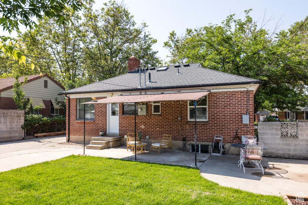 Back of property featuring a patio, a chimney, a shingled roof, and brick siding