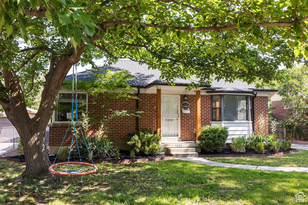 View of front of property featuring brick siding, roof with shingles, and a front lawn