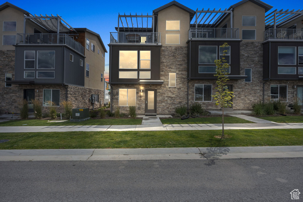 Townhome / multi-family property with a balcony, stucco siding, a front lawn, and stone siding