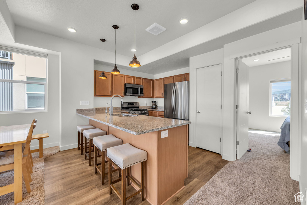 Kitchen with appliances with stainless steel finishes, brown cabinets, a peninsula, a kitchen bar, and light wood finished floors