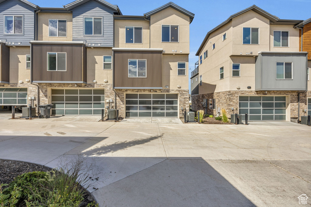 View of front of house with an attached garage, driveway, stone siding, and stucco siding