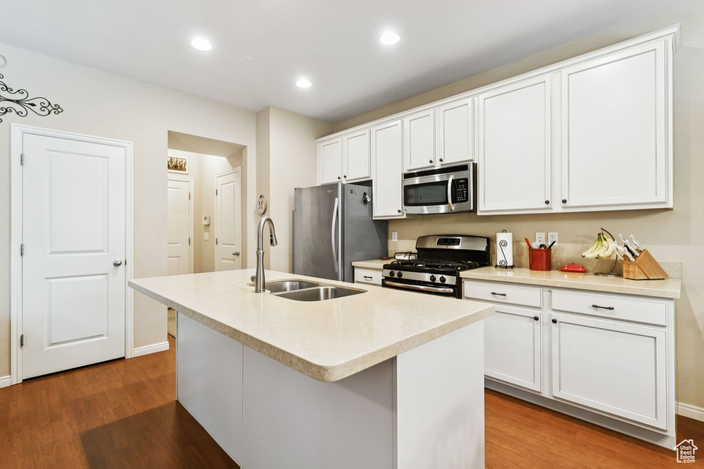 Kitchen with appliances with stainless steel finishes, wood finished floors, a kitchen island with sink, recessed lighting, and white cabinetry