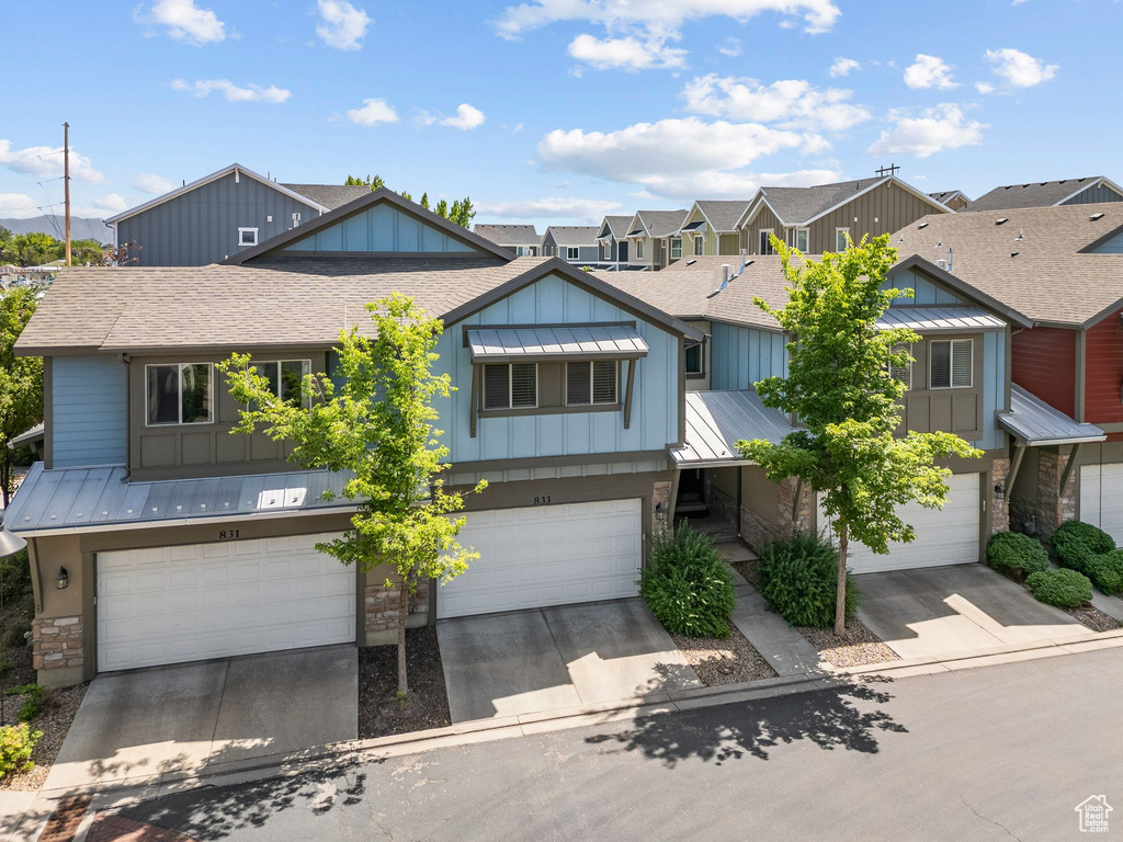 Townhome / multi-family property with a standing seam roof, an attached garage, roof with shingles, driveway, and board and batten siding