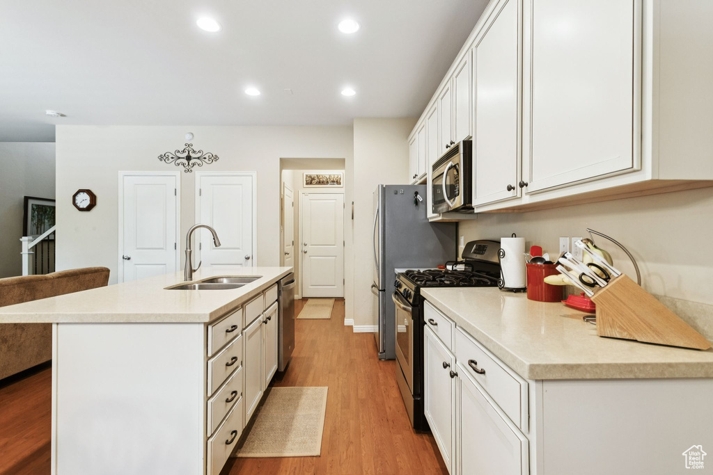 Kitchen with appliances with stainless steel finishes, white cabinets, a kitchen island with sink, light wood finished floors, and recessed lighting