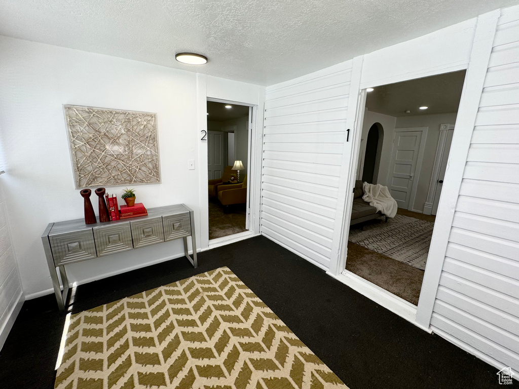 Corridor featuring dark colored carpet, arched walkways, and a textured ceiling