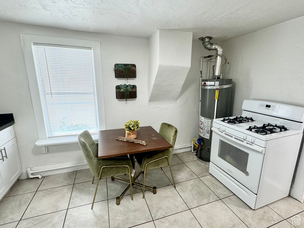 Kitchen with white gas range, secured water heater, white cabinetry, a textured ceiling, and light tile patterned floors
