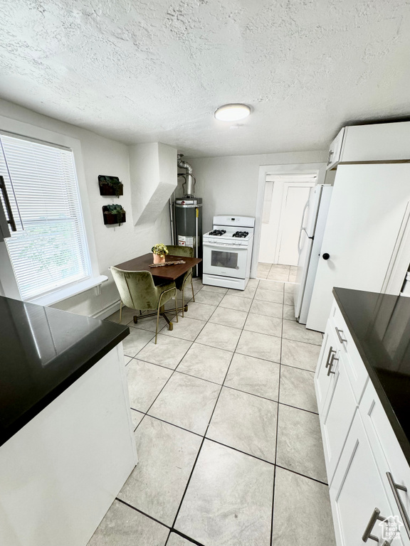 Kitchen featuring white appliances, water heater, dark countertops, white cabinets, and light tile patterned floors