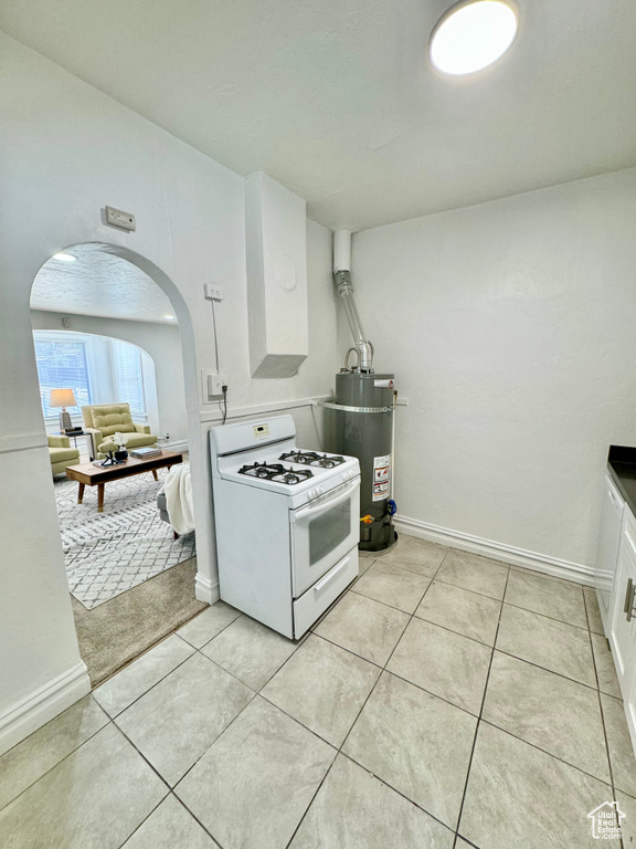 Kitchen with white gas range, arched walkways, secured water heater, white cabinetry, and light tile patterned floors