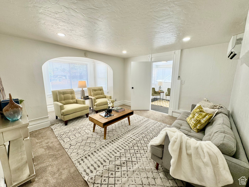 Carpeted living room featuring arched walkways, a wall mounted AC, plenty of natural light, recessed lighting, and a textured ceiling