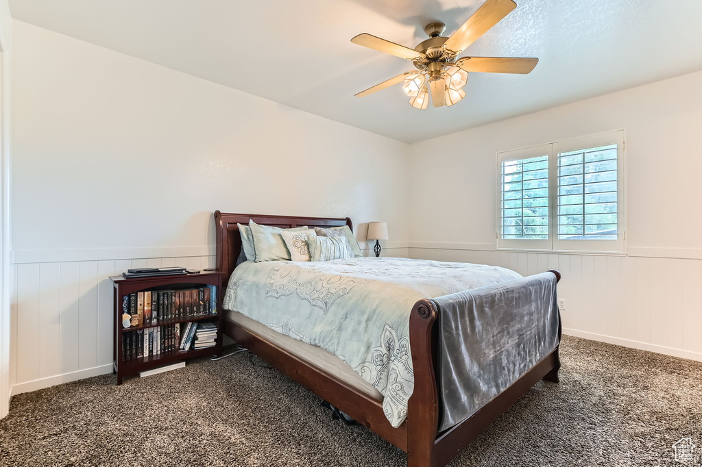 Carpeted bedroom featuring a wainscoted wall and a ceiling fan