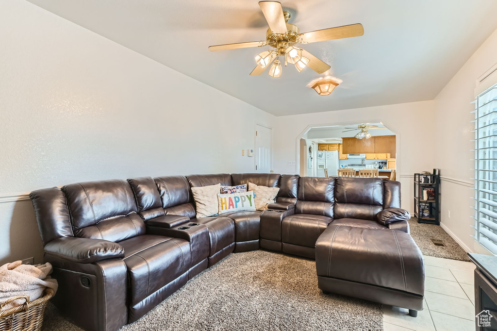 Living room featuring a ceiling fan, arched walkways, light tile patterned floors, and light carpet