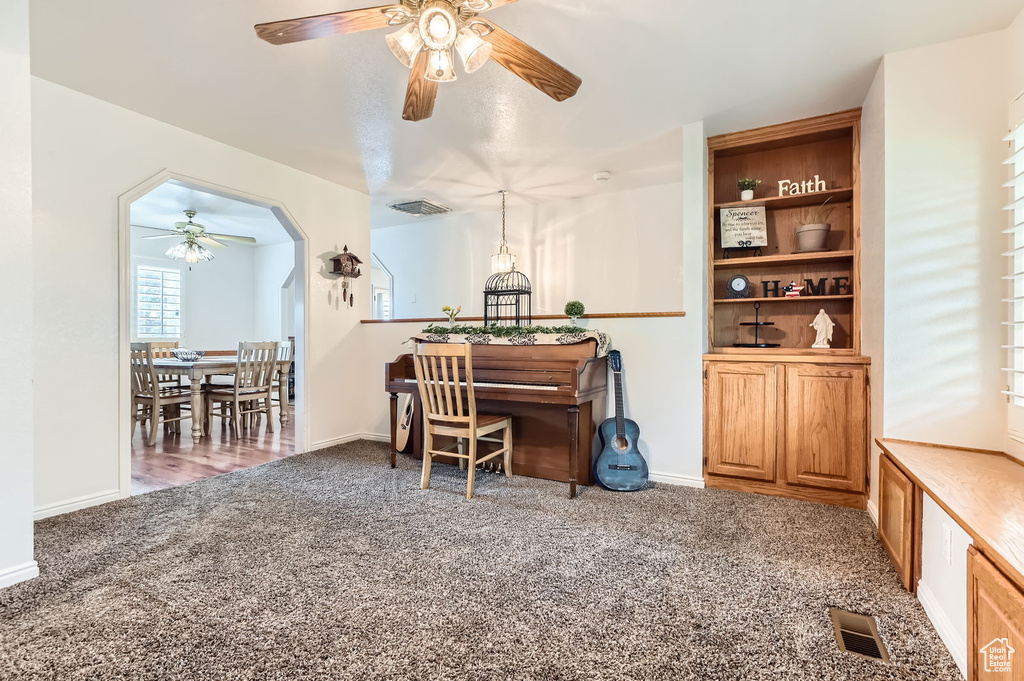 Carpeted office space featuring a ceiling fan and arched walkways