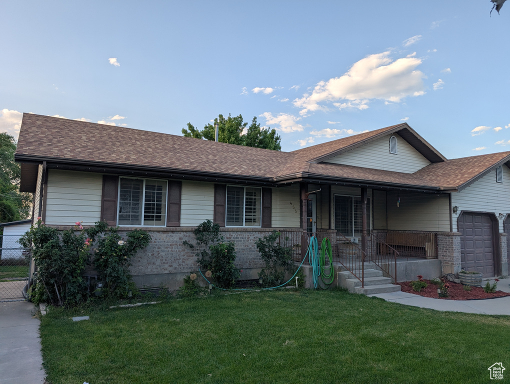 Ranch-style home with brick siding, covered porch, a front lawn, an attached garage, and roof with shingles