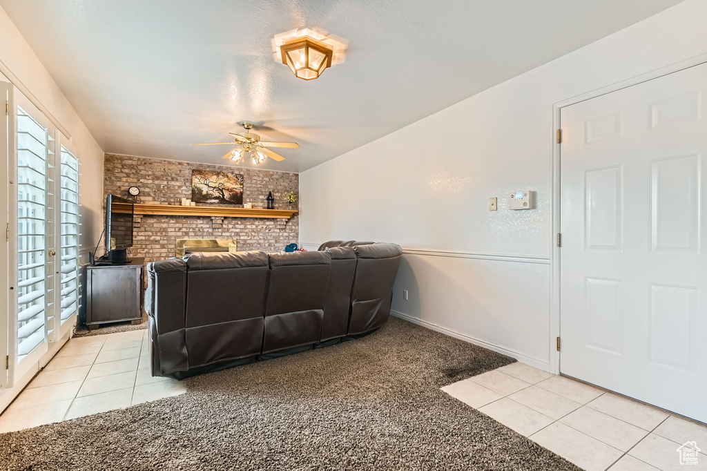 Living room featuring light tile patterned flooring, ceiling fan, light colored carpet, and brick wall