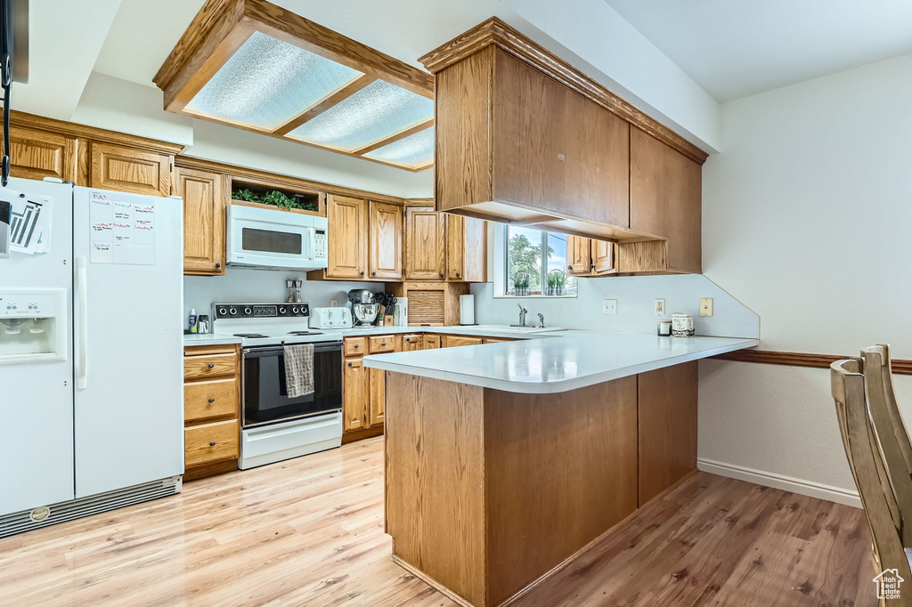 Kitchen featuring white appliances, a peninsula, light wood-style flooring, and light countertops