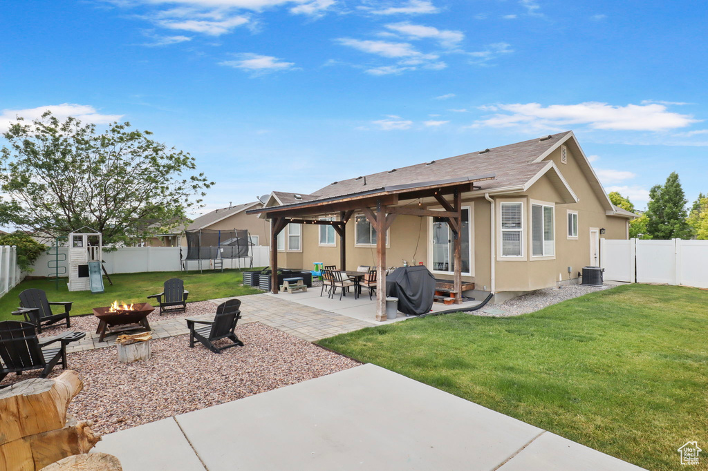 Back of property with an outdoor fire pit, a trampoline, a fenced backyard, and a patio
