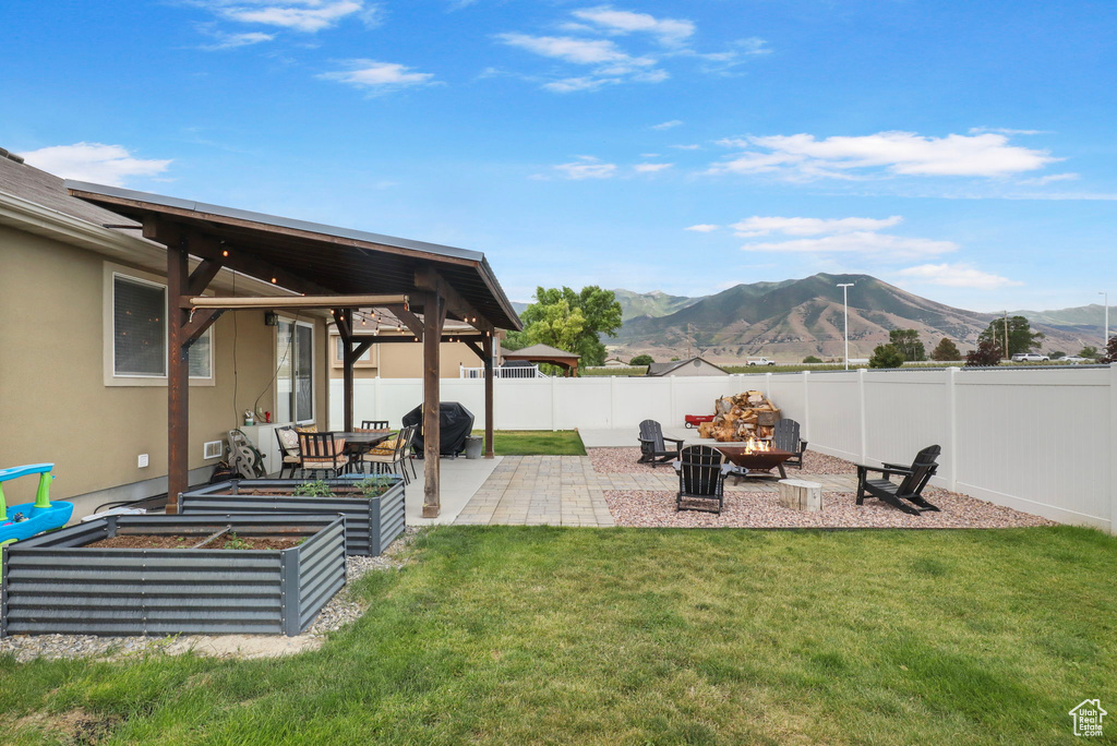 Fenced backyard with a mountain view, a patio, a vegetable garden, and an outdoor fire pit