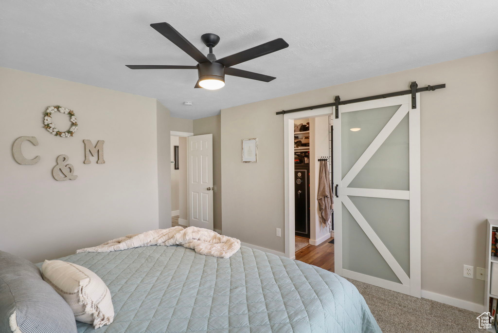 Bedroom with a barn door, a spacious closet, ceiling fan, carpet flooring, and a closet