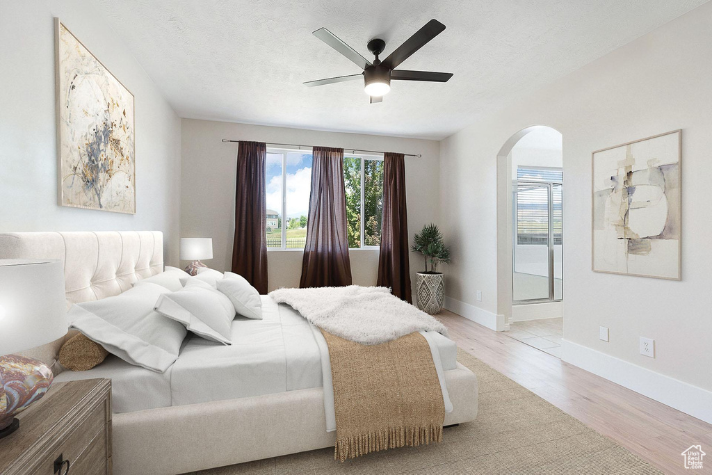 Bedroom with arched walkways, light wood-style floors, and a ceiling fan