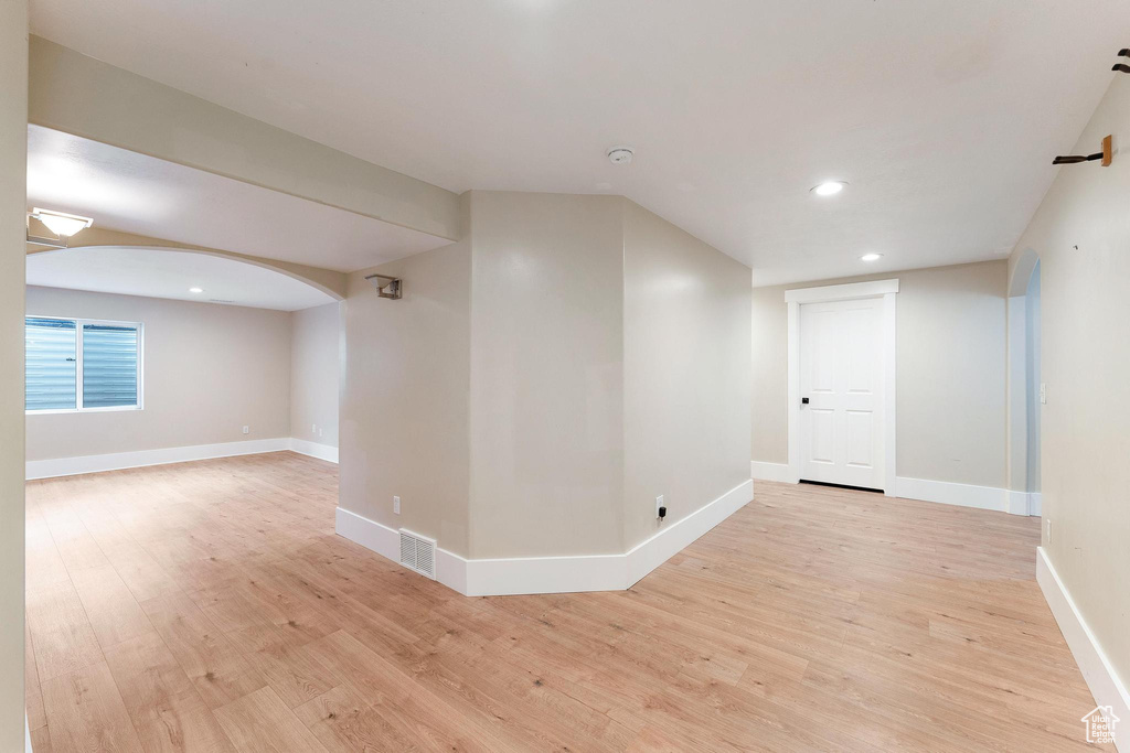 Empty room with light wood-style floors, recessed lighting, and arched walkways