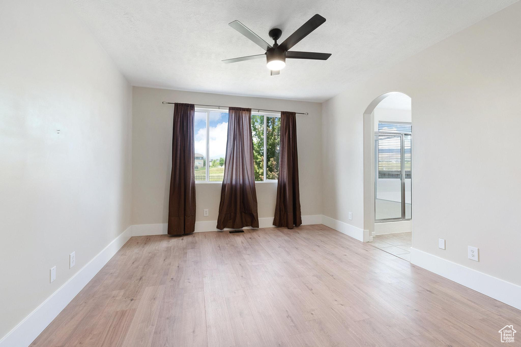 Spare room with arched walkways, ceiling fan, and light wood-style flooring