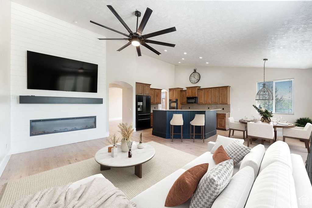 Living area with a textured ceiling, ceiling fan, light wood-style floors, a large fireplace, and arched walkways