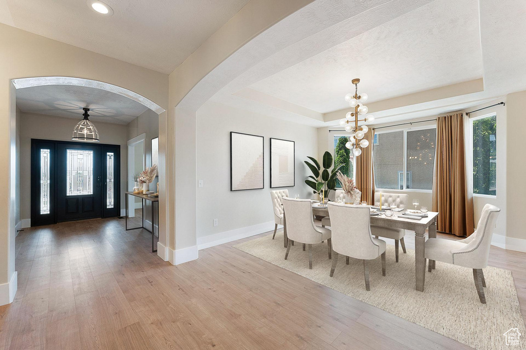 Dining space featuring a chandelier, light wood-style flooring, arched walkways, recessed lighting, and a tray ceiling