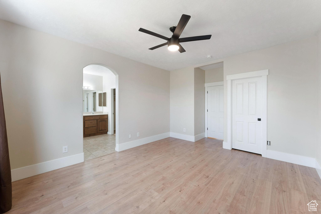Unfurnished room with arched walkways, a ceiling fan, and light wood-style floors